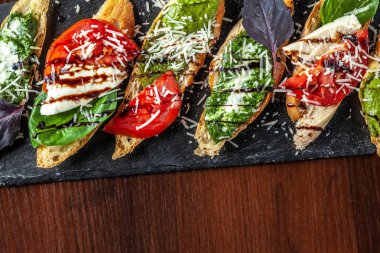 Mozzarella peyniri, domates, pesto sos ve parmesan peyniri, siyah bir taş, ahşap bir masa ile İtalyan bruschettes. Kopya alanı, seçici odak