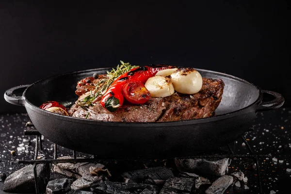 concept of the process of cooking meat. The steak is roasted on charcoal in a cast-iron frying pan, with spices, garlic, hot red pepper, squarish, thyme. image background. Copy space, selective focus