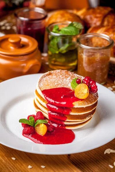 A stack of American pan cakes with jam and forest berries, in the restaurant for breakfast. in the background, jam with croissants. Copy space, selective focus