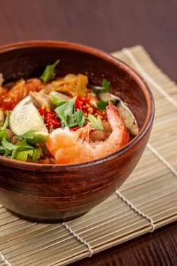 Asya Doğu mutfağı. Japon baharatlı çorba deniz ürünleri, karides, sebze, limon, maydanoz ve kırmızı kil, bir tabak içinde acı biber ile bir restoranda bir tablo üzerinde duruyor. Kopya alanı, seçici odak
