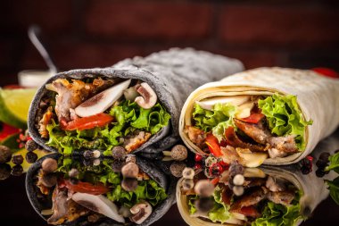 Two burrito, black and white lavash with chicken, mushrooms, salad, cherry tomatoes, lime, and salsa. Copy space, selective focus clipart