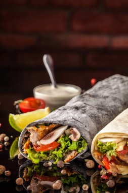 Two burrito, black and white lavash with chicken, mushrooms, salad, cherry tomatoes, lime, and salsa. Copy space, selective focus clipart