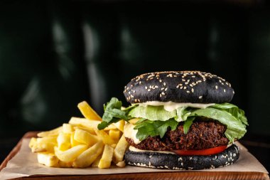 Siyah vejetaryen burger pirzola bezelye falafel, domates, salatalık, rucola salata ve patates kızartması. siyah bir arka plan üzerinde. Kopya alanı, seçici odak