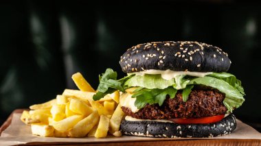 Siyah vejetaryen burger pirzola bezelye falafel, domates, salatalık, rucola salata ve patates kızartması. siyah bir arka plan üzerinde. Kopya alanı, seçici odak