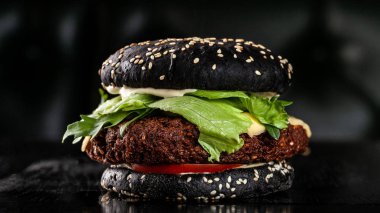 Siyah vejetaryen burger pirzola bezelye falafel, domates, salatalık, rucola salata ve patates kızartması. siyah bir arka plan üzerinde. Kopya alanı, seçici odak