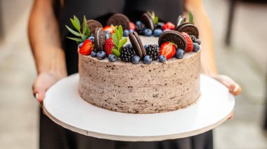 Kız bir pasta ile orman çilek, çilek, yaban mersini, şehirde sokakta tutuyor. Kek, pastaneler, restoranlar üretimi için bir kavram. Arka plan resmi