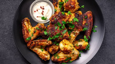 Baharat köri ve siyah bir arka plan üzerinde siyah bir tabakta maydanoz ile Meksika pişmiş tavuk kanatları. yan görünüm, kopya alanı, üstten görünüm