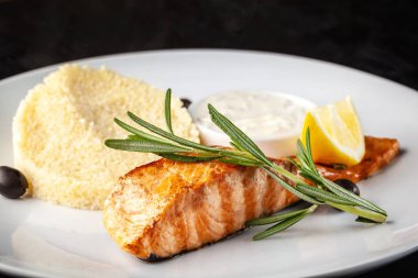 Kızarmış biftek kırmızı balık alabalık veya biberiye ile somon ızgara, yulaf lapası ve limon beyaz tabakta. Siyah bir masaya. arka plan görüntüsü. Kopya alanı