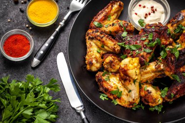 Baharat köri ve siyah bir arka plan üzerinde siyah bir tabakta maydanoz ile Meksika pişmiş tavuk kanatları. yan görünüm, kopya alanı, üstten görünüm