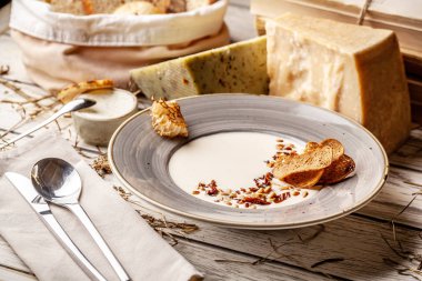 Kurutulmuş domates ve çam fıstığı ile İtalyan peynir krem çorbası. Tablo yanında Parmesan peyniri ve Dor-mavi, Beyaz ahşap bir masa üzerinde başıdır.