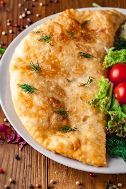 Özbek Doğu Tatar mutfağı, et ve suluguni ile cheburek peynirli sebze ve Yeşiller ahşap bir masa üzerinde beyaz bir tabak içinde.