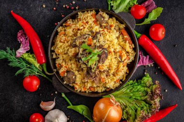 Uzbek Oriental cuisine. Pilaf in a cast-iron frying pan made of lamb. next to the vegetables on a black table. selective focus clipart