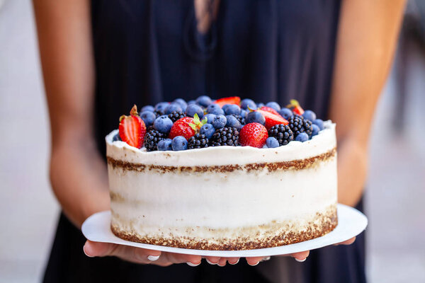 The girl is holding a cake with forest berries, strawberries, blueberries, on the street in the city. A concept for the production of cakes, bakeries, restaurants. Background image