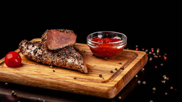 two juicy beef pepper steak with a air fryer medium rare, with a red sharp sauce on a wooden board, on a black background. Copy space