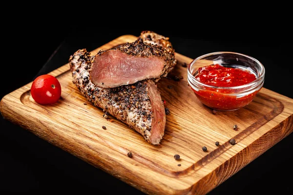 two juicy beef pepper steak with a air fryer medium rare, with a red sharp sauce on a wooden board, on a black background. Copy space