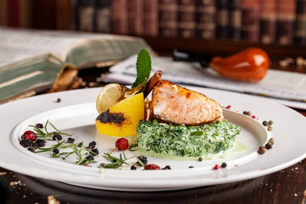 English cuisine. A steak of red fish salmon or trout lies on a pillow of spinach with cream, with lemon and cinnamon stick. Copy space, selective focus