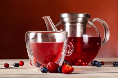 Orman meyveleri çift cam ve cam çaydanlık kırmızı bir arka plan üzerinde ahşap bir masa üzerinde bir fincan çay nane.