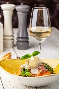 Sezar salatası somon. karışımı salata, domates, kaşar peyniri, fesleğen. Bir seramik tabak bir tabak bir restoranda ahşap bir masa var. Bir kadeh beyaz şarap tablodur. seçici odak