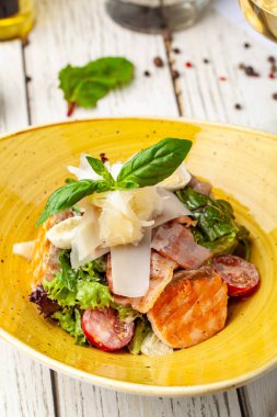 Sezar salatası somon. karışımı salata, domates, kaşar peyniri, fesleğen. Bir seramik tabak bir tabak bir restoranda ahşap bir masa var. Bir kadeh beyaz şarap tablodur. seçici odak