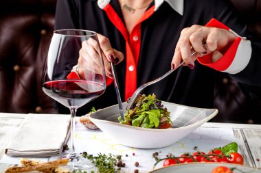 Kızın restoranında bir akşam yemeği, bir vejetaryen salata var. bıçak ve çatal elinde. Bir bardak kırmızı şarap tablodur