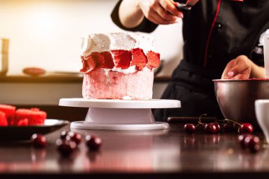 Kız Şef pudra bir kiraz ile bir petrol kek yapmak. Konsept üretim süreci evde sipariş müşterilerine kek. Kremalı pasta spatula smear. arka plan resmi.