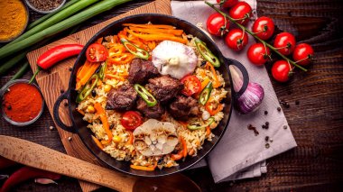Doğu özbek mutfağı kavramı. Ev yapımı pilav, koyun eti, Dana eti, tavuk, kuzu ile plov kazan, kimyon, kimyon, kiraz domates baharat yakınındaki ahşap bir gemide bir demir tavada kaplıdır