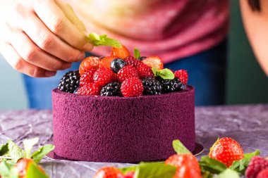 Şef aşçı pudra ellerinle yabani çilek, ahududu, çilek, yaban mersini ve nane ile Japon bisküvi bir pasta süsle. Arka plan görüntüsü. Kopya alanı