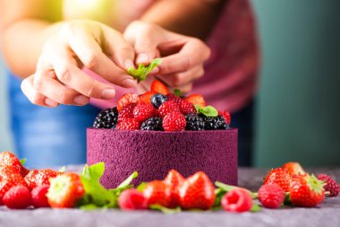 Şef aşçı pudra ellerinle yabani çilek, ahududu, çilek, yaban mersini ve nane ile Japon bisküvi bir pasta süsle. Arka plan görüntüsü. Kopya alanı