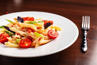 Domates ve fesleğen çatal yanındaki ahşap bir masa üzerinde bir beyaz forvor plaka ile domates soslu penne makarna. Arka plan görüntüsü. İtalyan makarna tarifleri için kavramı. kopya alanı, üstten görünüm