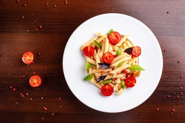 Domates ve fesleğen çatal yanındaki ahşap bir masa üzerinde bir beyaz forvor plaka ile domates soslu penne makarna. Arka plan görüntüsü. İtalyan makarna tarifleri için kavramı. kopya alanı, üstten görünüm