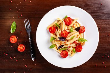 Domates ve fesleğen çatal yanındaki ahşap bir masa üzerinde bir beyaz forvor plaka ile domates soslu penne makarna. Arka plan görüntüsü. İtalyan makarna tarifleri için kavramı. kopya alanı, üstten görünüm
