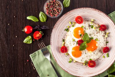 Sağlıklı beslenme kavramı. Sporcular için protein. Turistik kahvaltı. Kızarmış yumurta yalan bir el yapımı seramik tabak, çatal, cherry domates, fesleğen. Siyah arka plan. Kopya alanı, üstten görünüm.