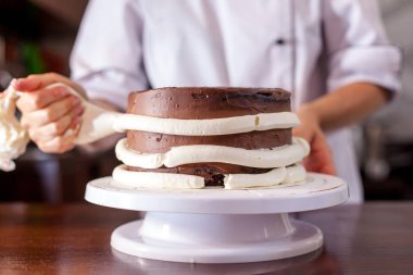 Pasta şefi, kendi elleriyle bir düğün pastası yapar ve onu meyveler ve çiçekler ile süsler. Arka plan görüntüsü. Uzay kopyalayın. Seçici odak.