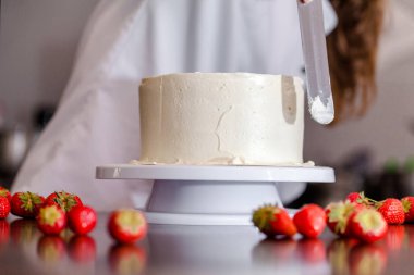 Pasta şefi, kendi elleriyle bir düğün pastası yapar ve onu meyveler ve çiçekler ile süsler. Arka plan görüntüsü. Uzay kopyalayın. Seçici odak.