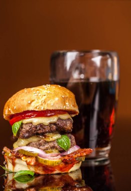 Amerikan fast food konsepti. Sulu bir Amerikan hamburgeri, iki biftek köftesi ve cam bir masada koyu bir bira ve turuncu bir arka plan. Boşluğu kopyala