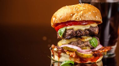 Amerikan fast food konsepti. Sulu bir Amerikan hamburgeri, iki biftek köftesi ve cam bir masada koyu bir bira ve turuncu bir arka plan. Boşluğu kopyala