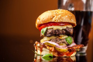 Amerikan fast food konsepti. Sulu bir Amerikan hamburgeri, iki biftek köftesi ve cam bir masada koyu bir bira ve turuncu bir arka plan. Boşluğu kopyala