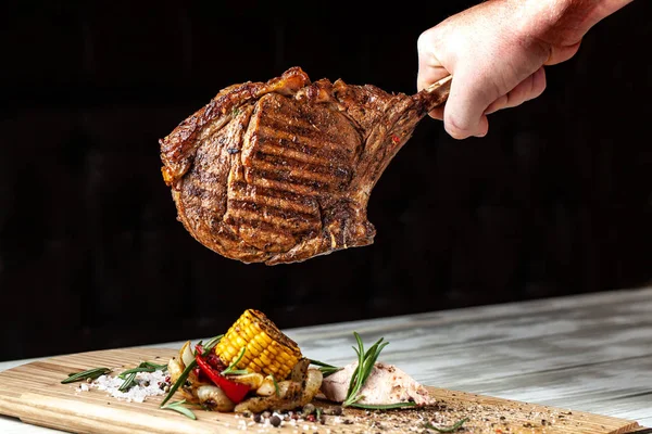 Koyun eti biftek, domuz eti, Dana eti veya sığır eti kemik üzerinde büyük bir kavrulmuş parça şefin Şef, elinde bir hava fritöz üzerinde siyah bir zemin üzerine bir arka plan görüntüsü pişmiş.