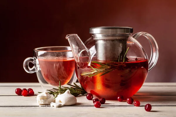 Mint tea with forest berries in a cup of double glass and a glass teapot on a wooden table, on a red background.
