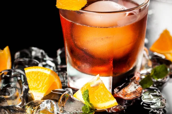 A cool orange alcohol cocktail with an ice ball in a glass on the bar. on the table, ice, orange, mint. Concept background image for bars, cafes.
