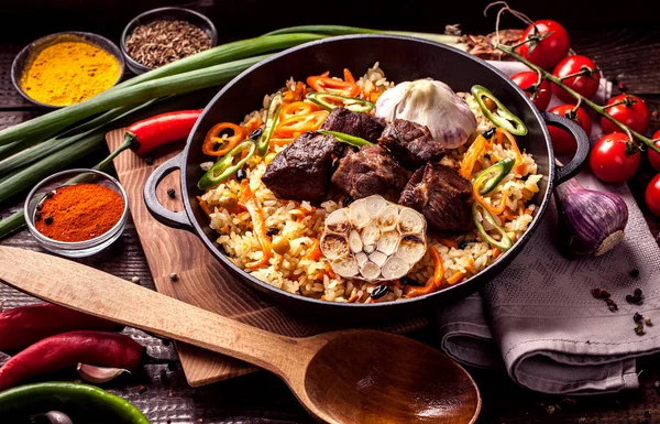 Doğu özbek mutfağı kavramı. Ev yapımı pilav, koyun eti, Dana eti, tavuk, kuzu ile plov kazan, kimyon, kimyon, kiraz domates baharat yakınındaki ahşap bir gemide bir demir tavada kaplıdır