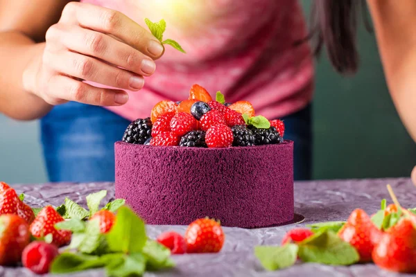 The chef cook confectioner decorates hands with a cake from Japanese biscuit with wild berries, raspberries, strawberries, blueberries and mint. Background image. Copy space
