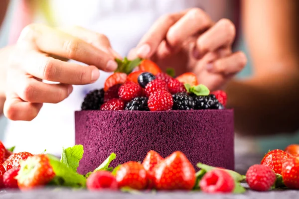 The chef cook confectioner decorates hands with a cake from Japanese biscuit with wild berries, raspberries, strawberries, blueberries and mint. Background image. Copy space