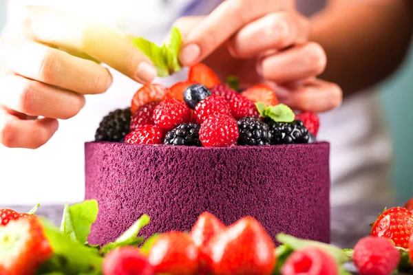 The chef cook confectioner decorates hands with a cake from Japanese biscuit with wild berries, raspberries, strawberries, blueberries and mint. Background image. Copy space