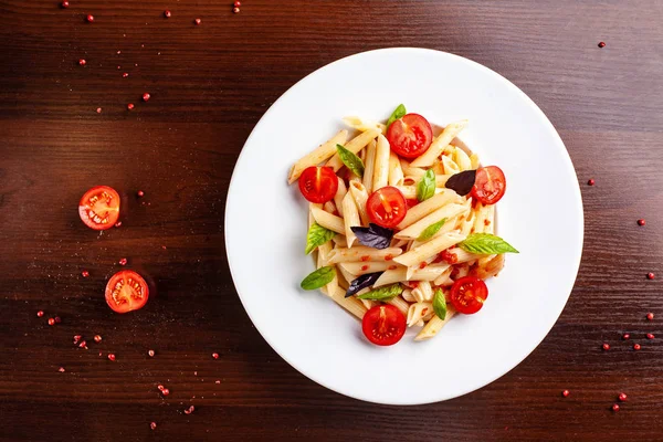 Domates ve fesleğen çatal yanındaki ahşap bir masa üzerinde bir beyaz forvor plaka ile domates soslu penne makarna. Arka plan görüntüsü. İtalyan makarna tarifleri için kavramı. kopya alanı, üstten görünüm