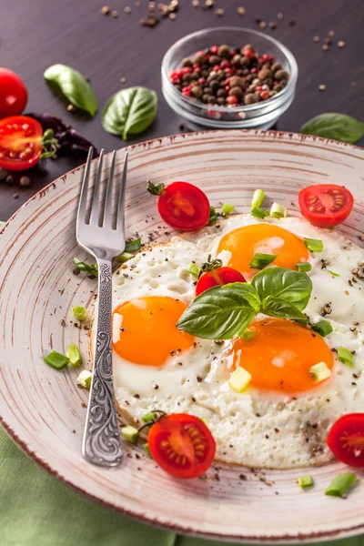 Concept of healthy eating. Protein for athletes. Tourist breakfast. Fried eggs lie on a handmade ceramic plate, fork, cherry tomatoes, basil. Black background. Copy space, top view.