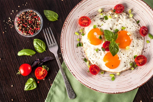 Concept of healthy eating. Protein for athletes. Tourist breakfast. Fried eggs lie on a handmade ceramic plate, fork, cherry tomatoes, basil. Black background. Copy space, top view.