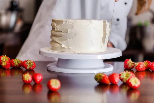Pastry chef, makes a wedding cake with his own hands and decorates him with berries and flowers. Background image. Copy space. Selective focus.