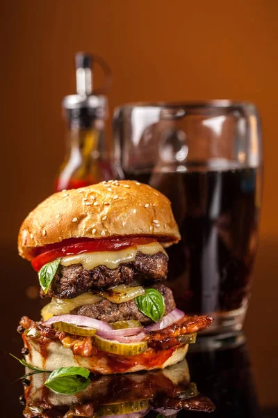 Amerikan fast food konsepti. Sulu bir Amerikan hamburgeri, iki biftek köftesi ve cam bir masada koyu bir bira ve turuncu bir arka plan. Boşluğu kopyala