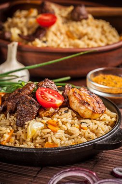 Doğu, özbek mutfağı kavramı. Biber pilav, plov bir siyah dökme demir tavada yalan malzemeler, soğan, domates, maydanoz, yanındaki ahşap bir masa üzerinde. Orta Asya mutfağı.